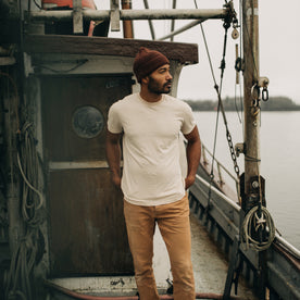 fit model standing on an old boat in The Cotton Hemp Tee in Sand, Knits by Taylor Stitch