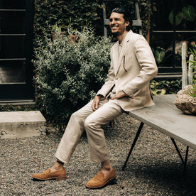 fit model sitting on a wooden table in The Sheffield Trouser in Natural Linen, Bottoms by Taylor Stitch