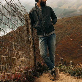 fit model wearing The Democratic Jean in in 18 Month Wash Organic Selvage, leaning against fence, Bottoms by Taylor Stitch