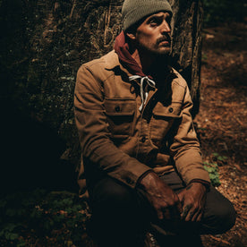 fit model wearing The Shop Shirt in Tobacco Boss Duck, sitting against tree, Wovens by Taylor Stitch