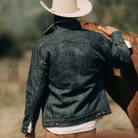 fit model wearing The Lined Long Haul Jacket in Green Cast Denim showing back while petting horse, Outerwear by Taylor Stitch