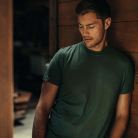 fit model leaning against the wall wearing The Cotton Hemp Tee in Pine, Knits by Taylor Stitch