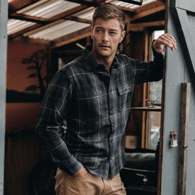 fit model leaning against a door in The Moto Utility Shirt in Shale Plaid, Wovens by Taylor Stitch