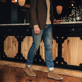 fit model leaning against a chair wearing The Rambler Chukka in Mushroom Suede, Footwear by Taylor Stitch