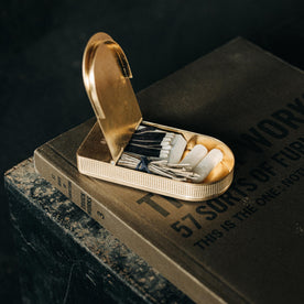 editorial image of The Tinder Box in Brass open with products inside on a book, Accessories by Taylor Stitch