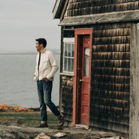 fit model wearing The Long Haul Jacket in Natural Organic Selvage, standing near red door, Outerwear by Taylor Stitch