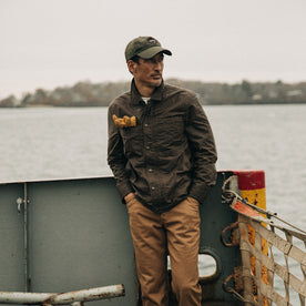 fit model wearing The Longshore Jacket in Dark Oak Waxed Canvas, near water, looking right, Outerwear by Taylor Stitch