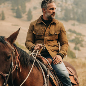 fit model wearing The Lined Long Haul Jacket in Harvest Tan Dry Wax, on horse, looking right, Outerwear by Taylor Stitch