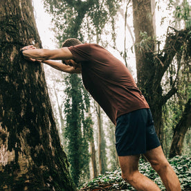 fit model wearing The Merino Tee in Wine, stretching against tree, Knits by Taylor Stitch